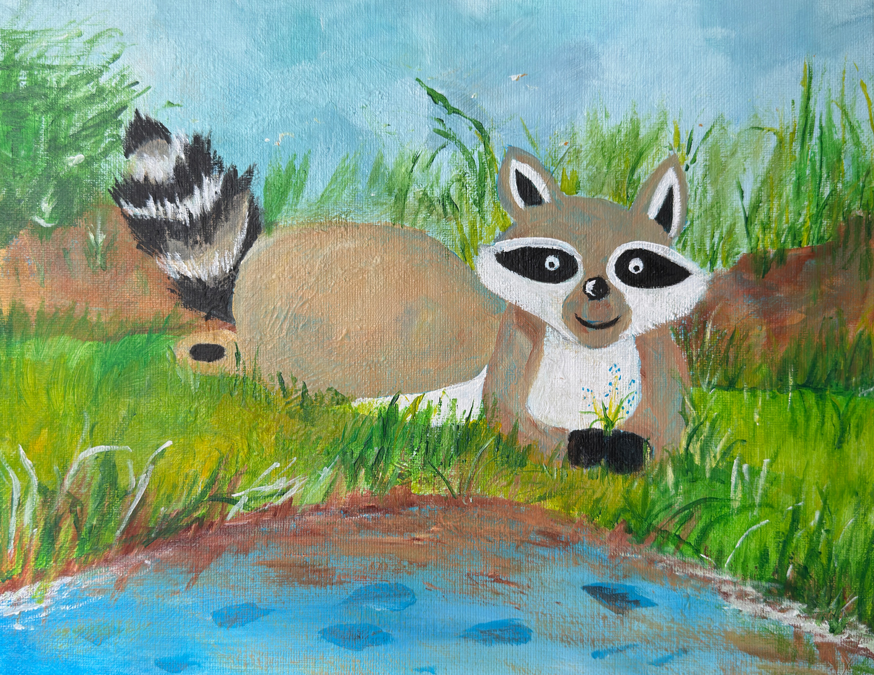 A smiling raccoon rests in green grass beside blue water, with its striped tail raised behind it.